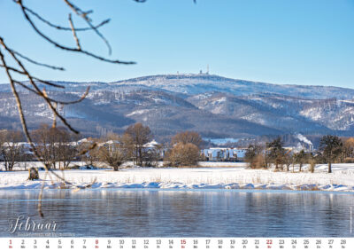 Schneebedeckter Brocken im Winter mit Wasser im Vordergrund.