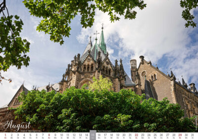 Gotische Schlosskirche Wernigerode hinter grünen Bäumen unter wolkigem Himmel